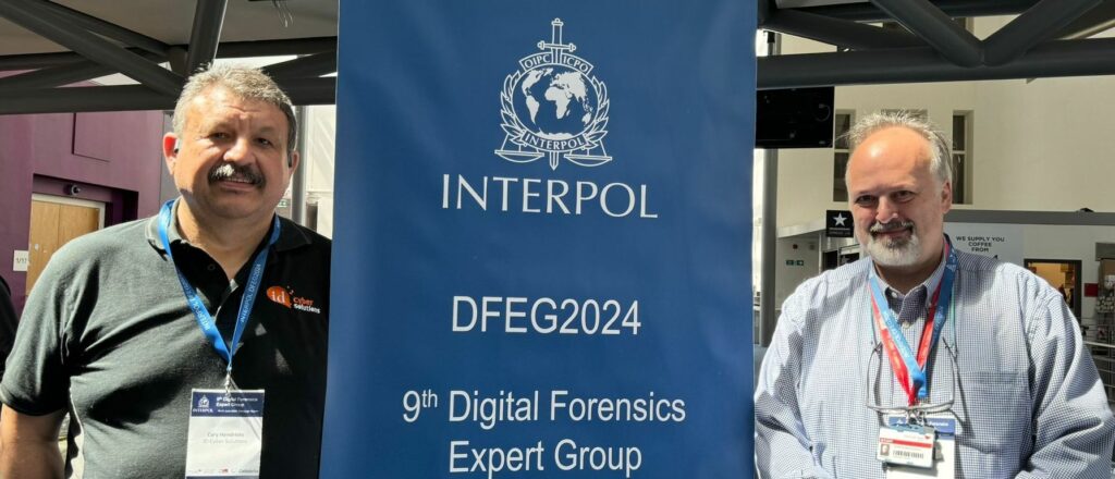 Cary and Basil standing beside a pop-up banner that says 'Interpol, DFEG 2024, 9th Digital Forensics Expert Group'.